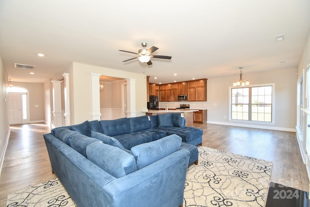 living room featuring light hardwood / wood-style floors, sink, ceiling fan with notable chandelier, and decorative columns