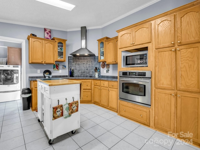 kitchen featuring washer / dryer, ornamental molding, wall chimney range hood, and stainless steel appliances