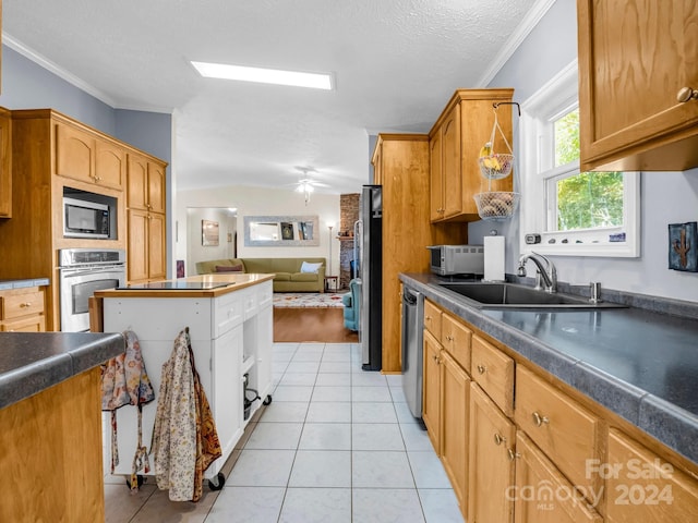 kitchen featuring ceiling fan, appliances with stainless steel finishes, light tile patterned floors, crown molding, and sink