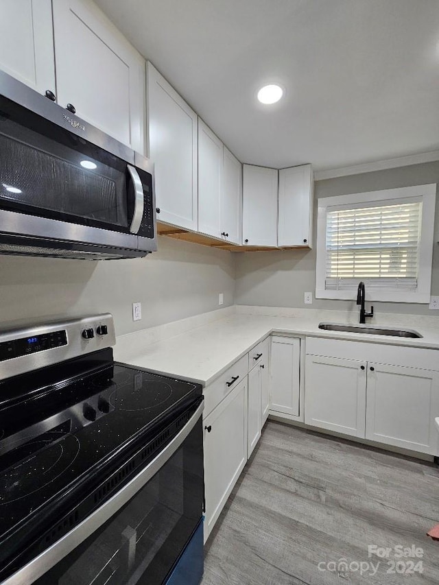 kitchen with appliances with stainless steel finishes, sink, white cabinetry, ornamental molding, and light hardwood / wood-style flooring