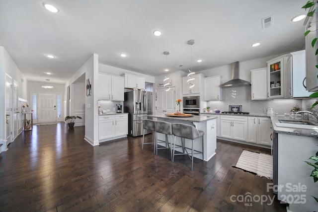 kitchen with a breakfast bar area, stainless steel appliances, a sink, a kitchen island, and wall chimney exhaust hood