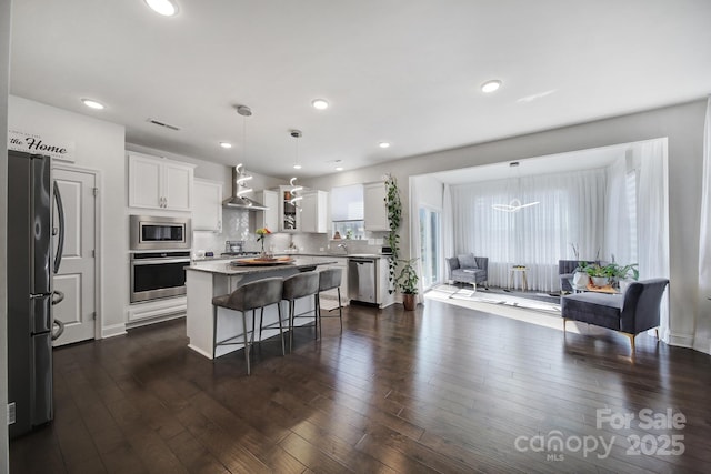 kitchen with stainless steel appliances, dark wood finished floors, wall chimney range hood, a center island, and a kitchen bar