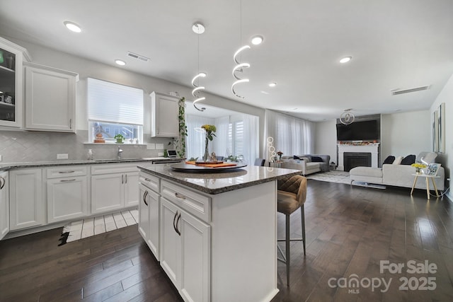 kitchen featuring visible vents, dark wood finished floors, a breakfast bar area, a center island, and a fireplace