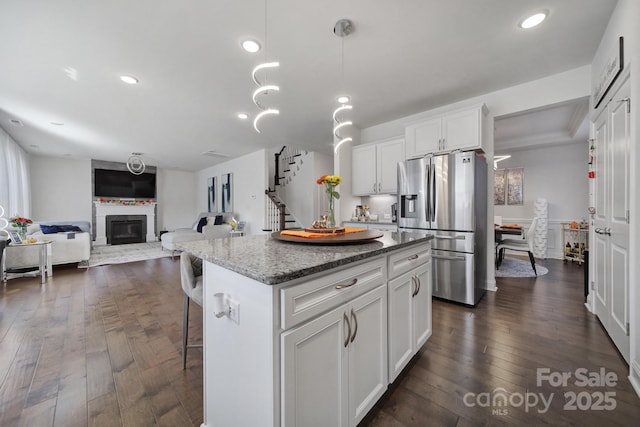 kitchen with white cabinets, a glass covered fireplace, stainless steel fridge with ice dispenser, dark wood-style floors, and a center island