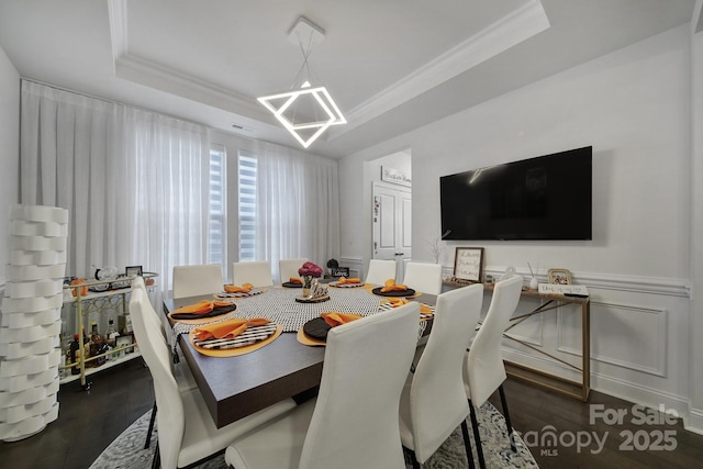 dining space featuring a raised ceiling, a wainscoted wall, wood finished floors, crown molding, and a decorative wall