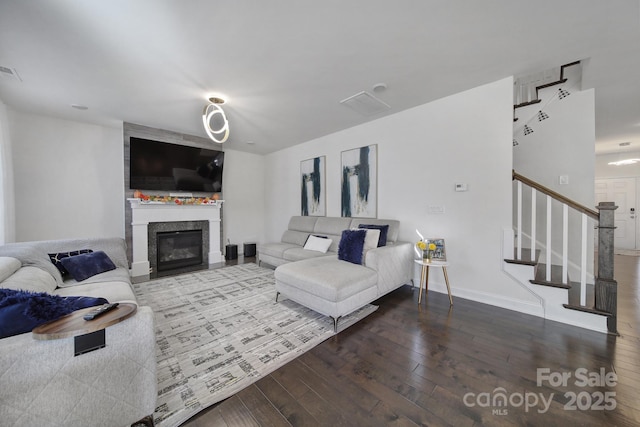 living area featuring visible vents, hardwood / wood-style floors, a glass covered fireplace, baseboards, and stairs