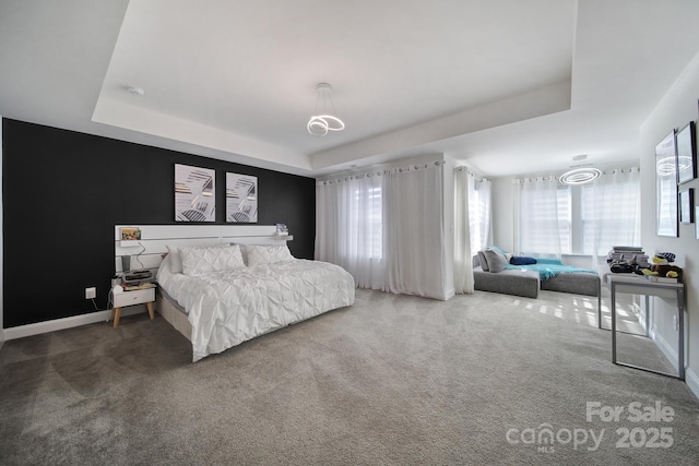 carpeted bedroom featuring a tray ceiling and baseboards