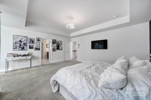 bedroom featuring a tray ceiling, light colored carpet, connected bathroom, and baseboards