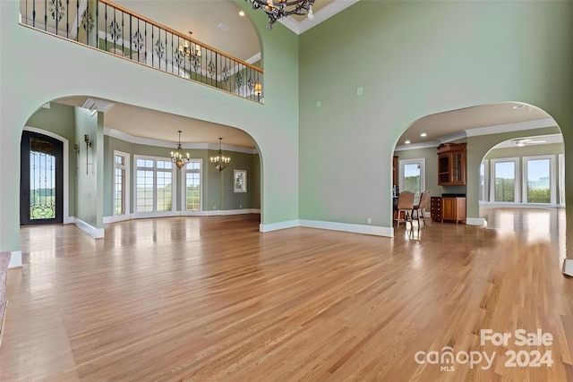 unfurnished living room featuring crown molding, a towering ceiling, and light hardwood / wood-style flooring