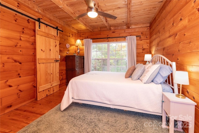 bedroom with wood ceiling, wood-type flooring, a barn door, and wood walls