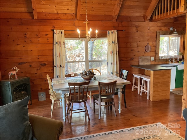 dining room with wooden walls, wood-type flooring, a wood stove, wood ceiling, and beam ceiling