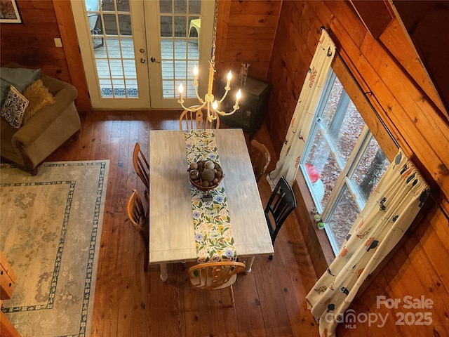 dining space with french doors, wood-type flooring, wooden walls, and a notable chandelier