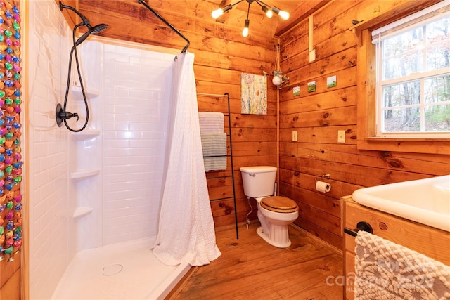 bathroom featuring hardwood / wood-style floors, wooden walls, vanity, toilet, and a shower with curtain