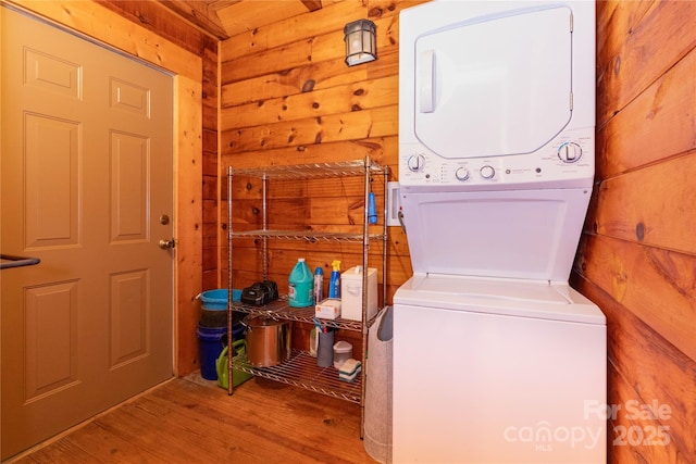 laundry area with wooden walls, wood-type flooring, and stacked washing maching and dryer