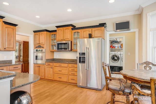 kitchen with dark stone counters, light wood-type flooring, washer and clothes dryer, appliances with stainless steel finishes, and ornamental molding