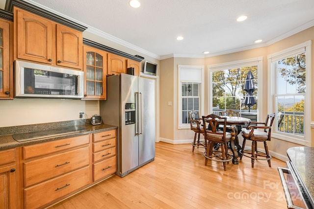 kitchen featuring stainless steel appliances, dark stone countertops, light wood-type flooring, a textured ceiling, and ornamental molding