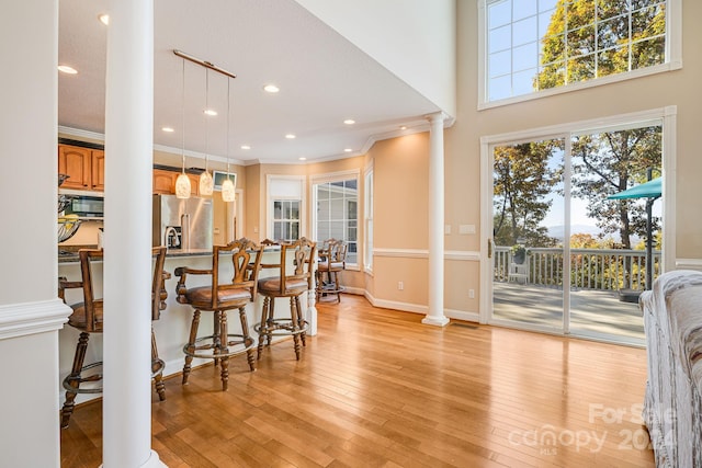 kitchen with appliances with stainless steel finishes, light wood-type flooring, ornate columns, crown molding, and hanging light fixtures