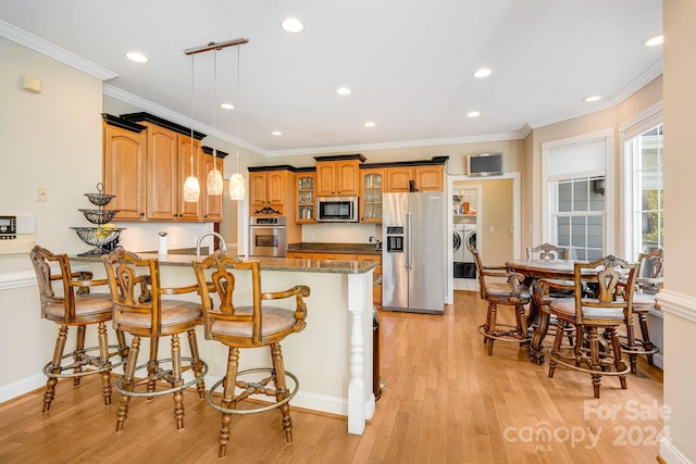 kitchen featuring pendant lighting, light hardwood / wood-style flooring, independent washer and dryer, appliances with stainless steel finishes, and a kitchen bar