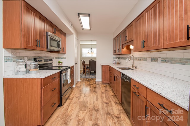 kitchen with appliances with stainless steel finishes, light stone countertops, sink, and light hardwood / wood-style floors