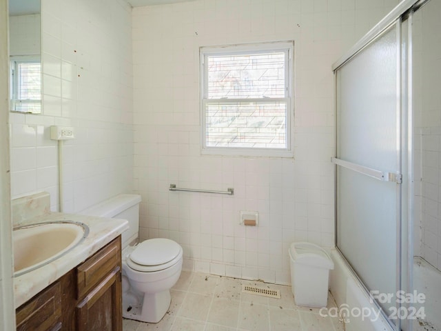 full bathroom featuring vanity, toilet, tile walls, and shower / bath combination with glass door