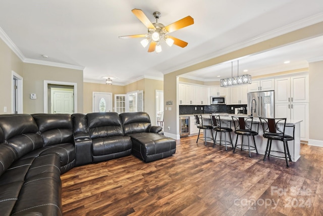 living room featuring beverage cooler, ceiling fan with notable chandelier, dark wood-type flooring, and crown molding