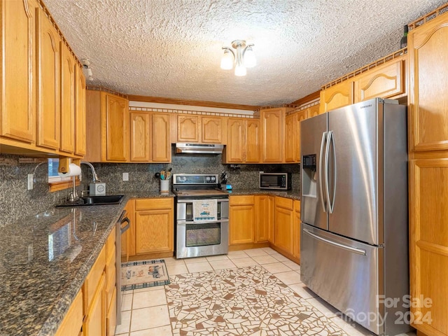 kitchen featuring dark stone counters, sink, light tile patterned floors, appliances with stainless steel finishes, and a textured ceiling