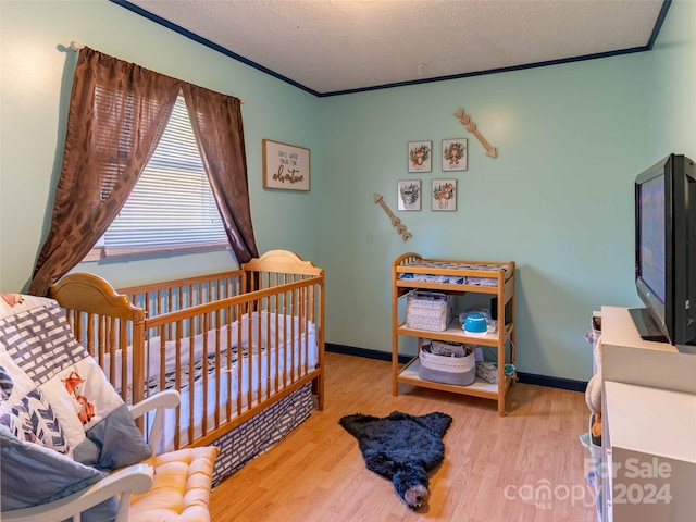 bedroom featuring a crib, crown molding, a textured ceiling, and hardwood / wood-style floors