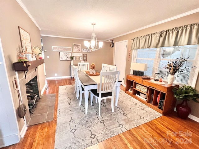 dining area with a tiled fireplace, crown molding, a notable chandelier, and light wood-type flooring