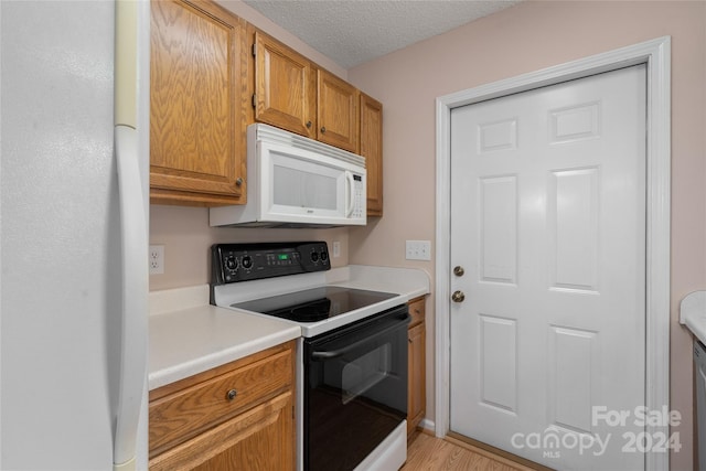 kitchen with white appliances, a textured ceiling, and light wood-type flooring