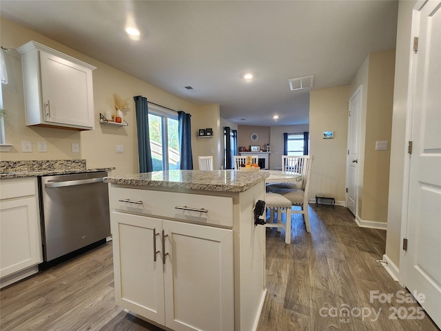 kitchen with light stone counters, dishwasher, a center island, white cabinetry, and wood-type flooring