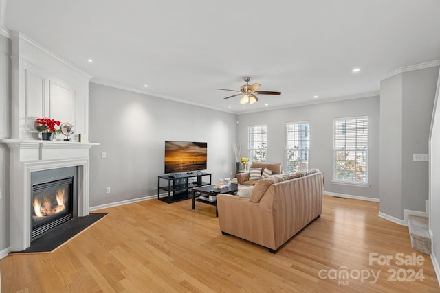 living room with ornamental molding, a fireplace, light wood-type flooring, and ceiling fan