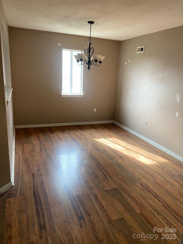 empty room with an inviting chandelier and dark wood-type flooring