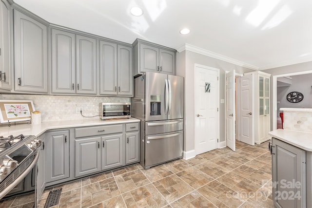 kitchen with gray cabinets, ornamental molding, stainless steel appliances, and backsplash