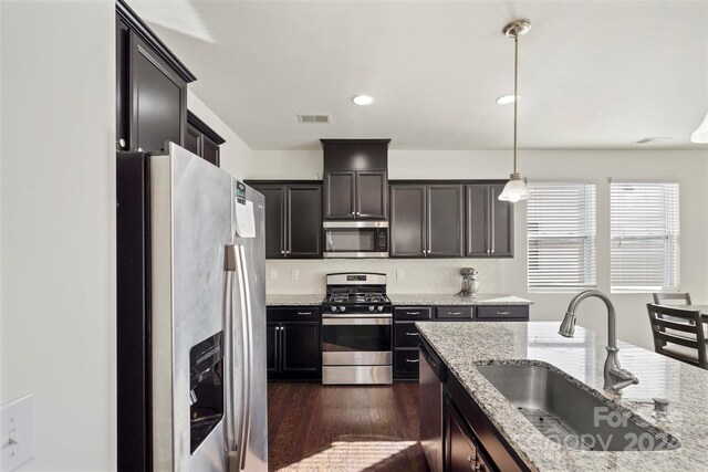 kitchen with appliances with stainless steel finishes, sink, pendant lighting, light stone counters, and dark hardwood / wood-style floors