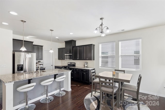 kitchen with dark hardwood / wood-style flooring, stainless steel appliances, hanging light fixtures, and an island with sink