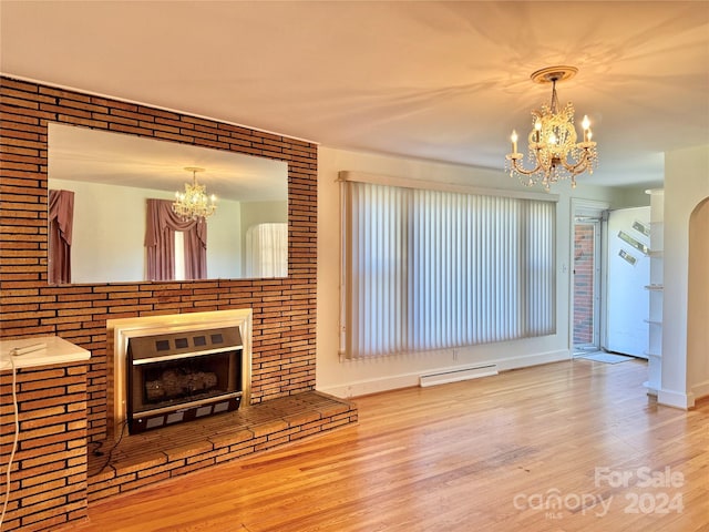 unfurnished living room featuring a chandelier, hardwood / wood-style floors, baseboard heating, and brick wall