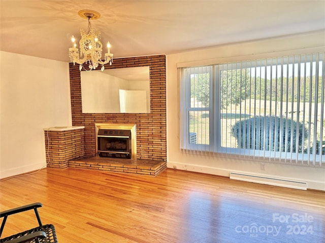 living room featuring hardwood / wood-style flooring, a brick fireplace, a baseboard heating unit, and a notable chandelier