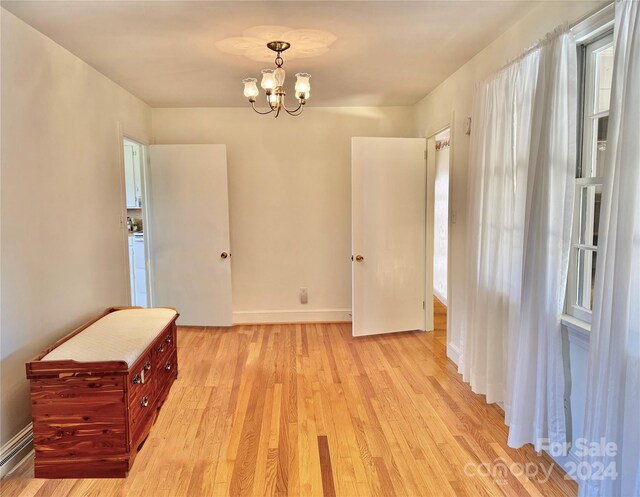 empty room featuring a chandelier, light hardwood / wood-style floors, and a baseboard heating unit