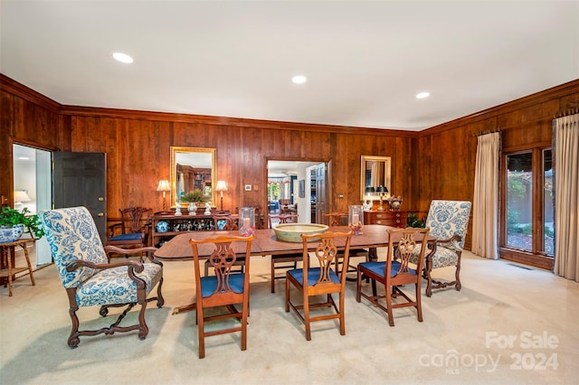 carpeted dining room with ornamental molding and wooden walls