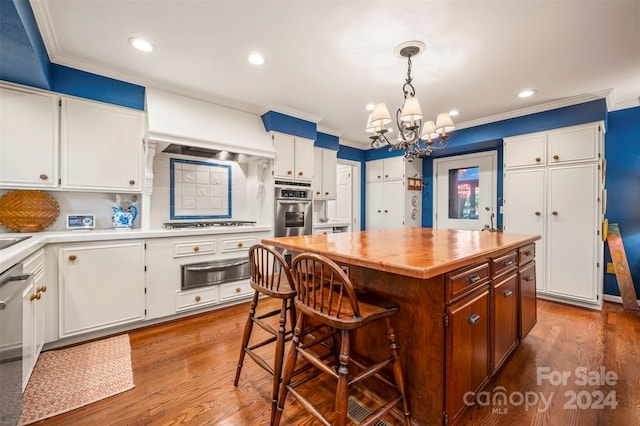 kitchen with white cabinets, a kitchen island, appliances with stainless steel finishes, hardwood / wood-style flooring, and crown molding