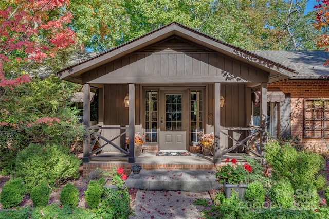 doorway to property with a porch, brick siding, and roof with shingles