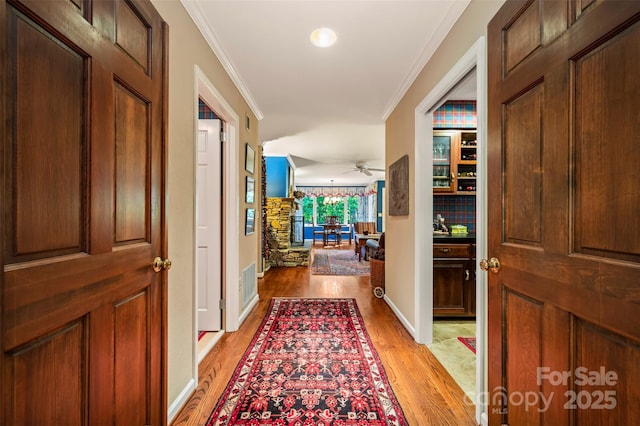 hall featuring crown molding, visible vents, light wood-type flooring, and baseboards