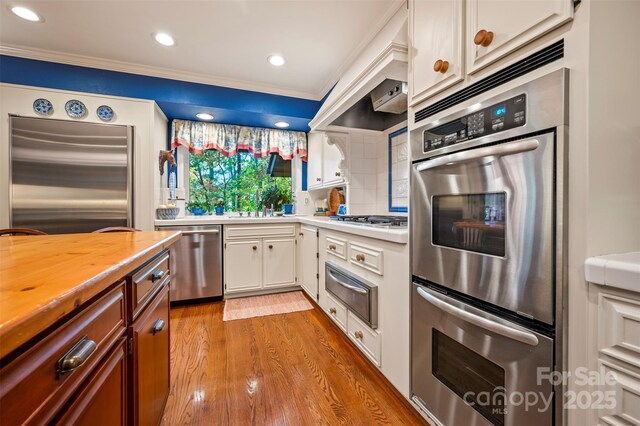 kitchen with light wood-style flooring, ornamental molding, stainless steel appliances, a warming drawer, and backsplash