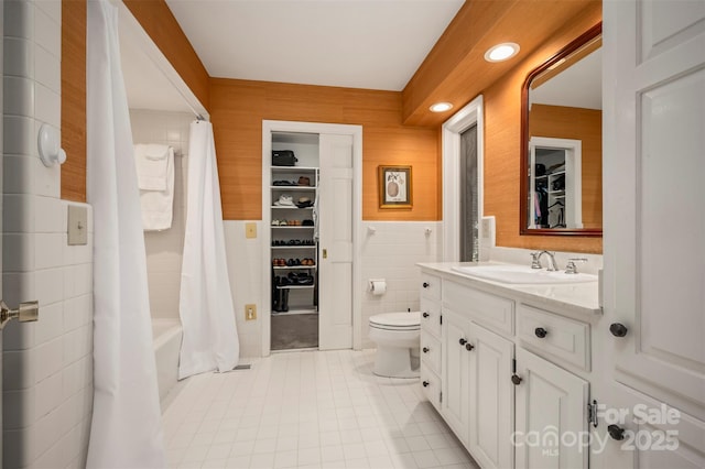 bathroom with a wainscoted wall, toilet, vanity, tile patterned floors, and tile walls