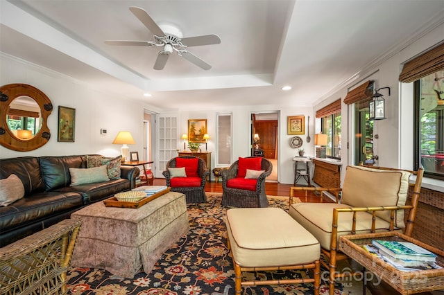 living area with crown molding, a raised ceiling, a ceiling fan, and wood finished floors