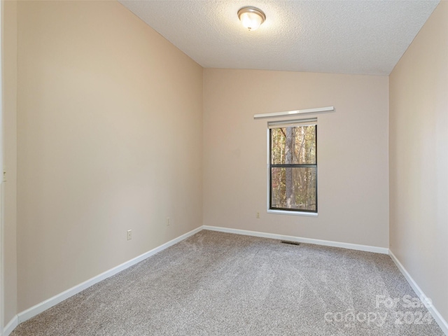 empty room featuring carpet, vaulted ceiling, baseboards, visible vents, and a textured ceiling