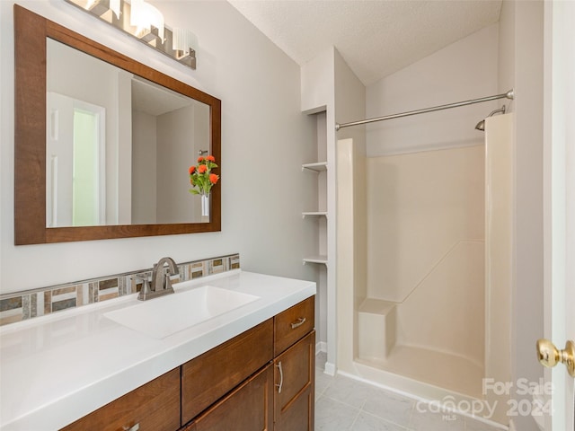full bath with vanity, tile patterned floors, vaulted ceiling, walk in shower, and a textured ceiling