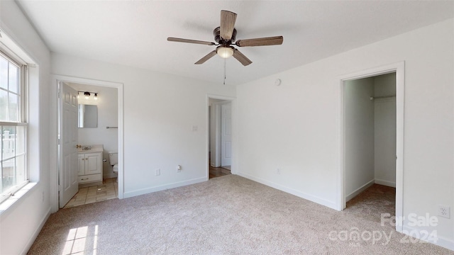 unfurnished bedroom featuring a closet, a spacious closet, light colored carpet, ensuite bathroom, and ceiling fan