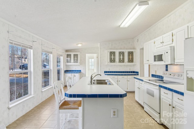 kitchen with white cabinetry, sink, a breakfast bar area, a kitchen island with sink, and white appliances