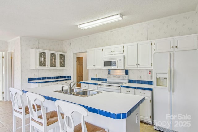 kitchen with a breakfast bar, sink, white cabinetry, a center island with sink, and white appliances